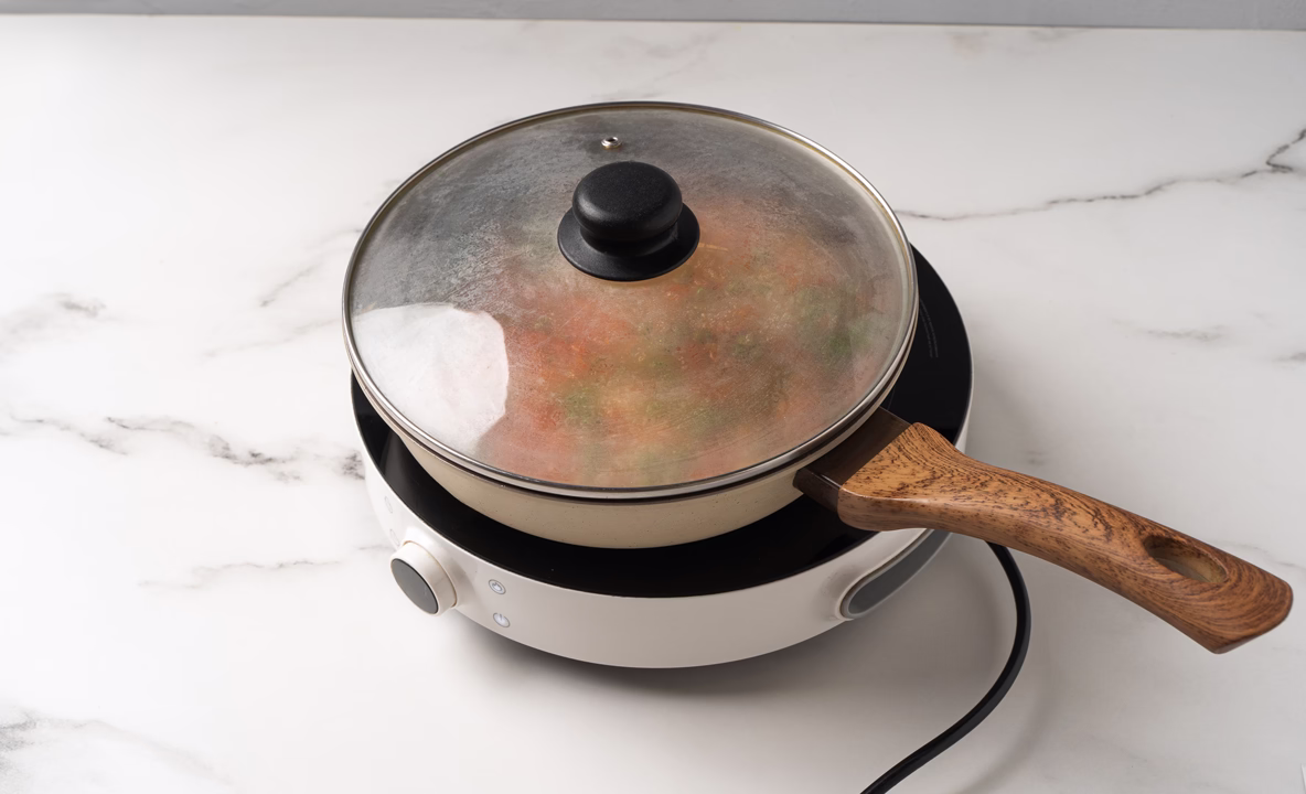 Овощи и рис на сковородке накрыты крышкой. 