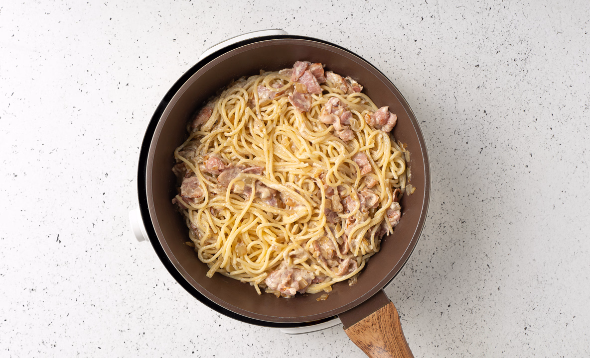 Макароны перемешаны с беконом и соусом в сковороде